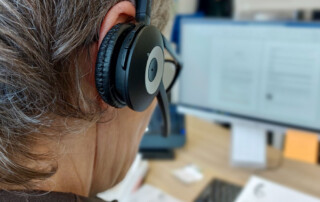 vrouw met headset, van achteren gefotografeerd met onscherp op de achtergrond twee beeldschermen