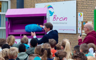 Wethouder Paul Boogaard gooit een zak textiel in de textielcontainer op het schoolplein van CBS De Bron in Numansdorp